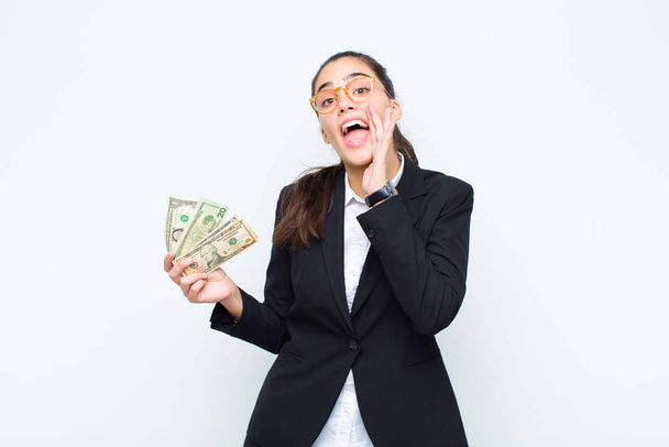 young businesswoman feeling happy, excited and positive, giving a big shout out with hands next to mouth, calling out with banknotes with bills - Фото, зображення