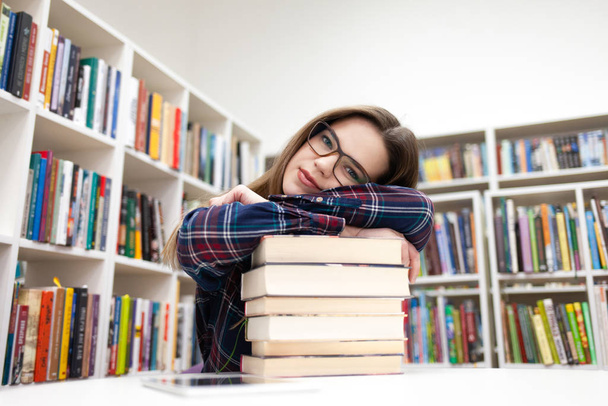 Mooie studente leunde haar hoofd op een stapel boeken. Jonge vrouw in bibliotheek concept - Foto, afbeelding