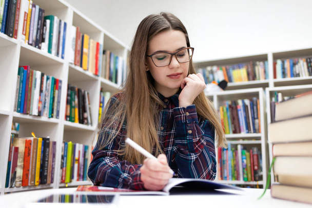  As raparigas escrevem na biblioteca. Jovem estudante estudando na biblioteca do campus
 - Foto, Imagem