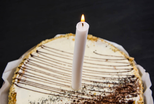 Tasty cake with a candle, condensed milk and poppy seeds on a plate on a black table. Close-up. - Foto, immagini