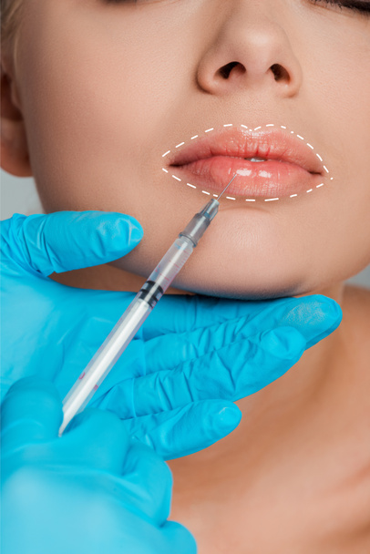 abgeschnittene Ansicht einer Kosmetikerin in Latex-Handschuhen, die einer Frau die Lippen vergrößert - Foto, Bild