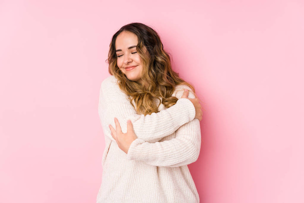 Mujer joven curvilínea posando en un fondo rosa abrazos aislados, sonriente despreocupado y feliz
. - Foto, imagen