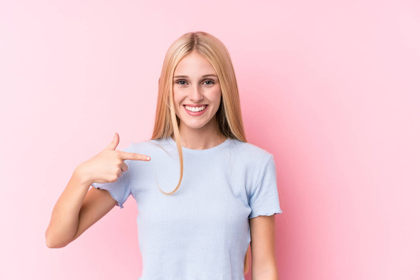 Nuori blondi nainen vaaleanpunainen tausta henkilö osoittaa käsin paita kopioi tilaa, ylpeä ja luottavainen
 - Valokuva, kuva