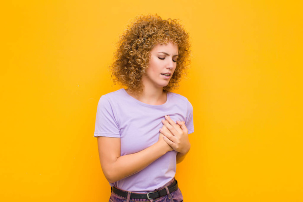 young afro woman looking sad, hurt and heartbroken, holding both hands close to heart, crying and feeling depressed against orange wall - Photo, Image