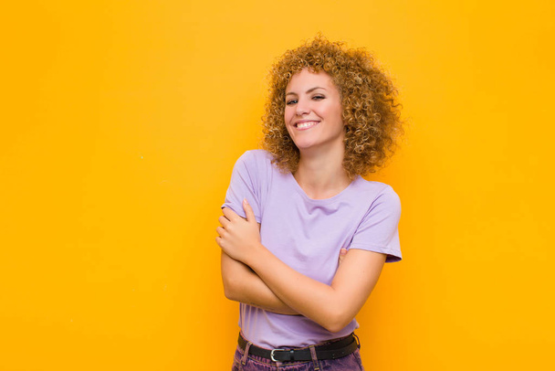 young afro woman laughing happily with arms crossed, with a relaxed, positive and satisfied pose against orange wall - Foto, Imagen