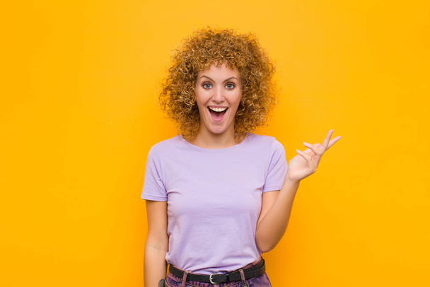 young afro woman feeling happy, surprised and cheerful, smiling with positive attitude, realizing a solution or idea against orange wall - Photo, Image