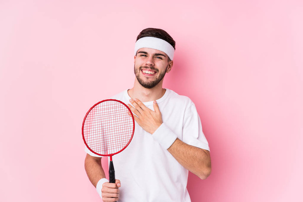 Jeune homme caucasien jouant au badminton isolé rit bruyamment en gardant la main sur la poitrine
. - Photo, image