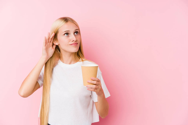 Молодая блондинка держит кофе на вынос, пытаясь слушать сплетни
. - Фото, изображение