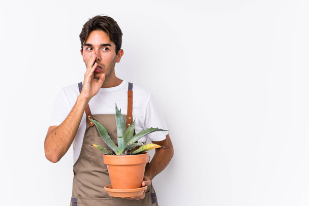 Молодий кавказький садівник, який тримає рослину ізольованою, каже таємні гарячі новини і дивиться вбік
 - Фото, зображення