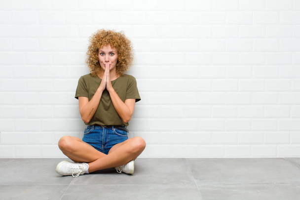 young afro woman happy and excited, surprised and amazed covering mouth with hands, giggling with a cute expression sitting on a floor - Fotografie, Obrázek