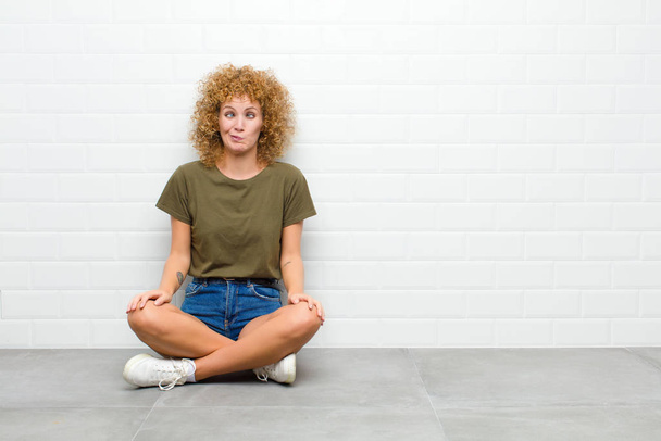 young afro woman looking goofy and funny with a silly cross-eyed expression, joking and fooling around sitting on a floor - Foto, imagen