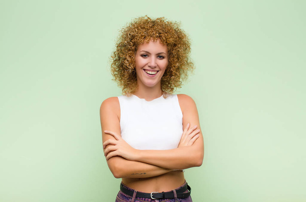 young afro woman looking like a happy, proud and satisfied achiever smiling with arms crossed against green wall - Фото, зображення
