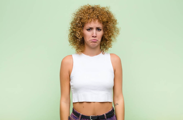 young afro woman feeling sad and whiney with an unhappy look, crying with a negative and frustrated attitude against green wall - Foto, imagen