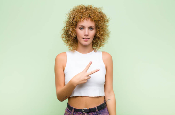 young afro woman feeling happy, positive and successful, with hand making v shape over chest, showing victory or peace against green wall - Foto, Bild