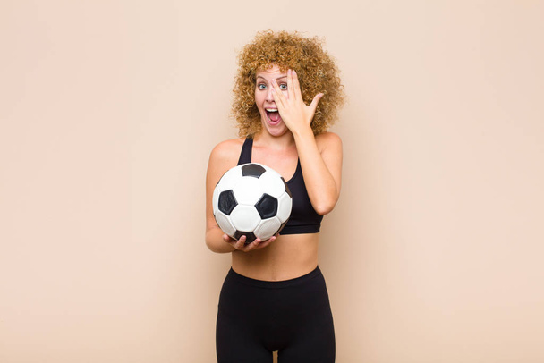 young afro woman covering face with hands, peeking between fingers with surprised expression and looking to the side sport concept - Foto, Imagem