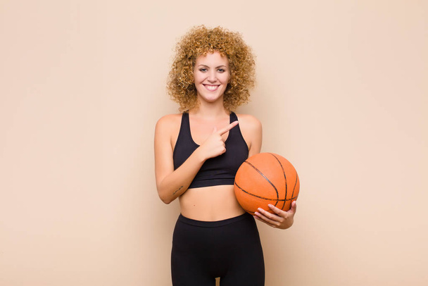 young afro woman smiling cheerfully, feeling happy and pointing to the side and upwards, showing object in copy space sport concept - Foto, Imagem