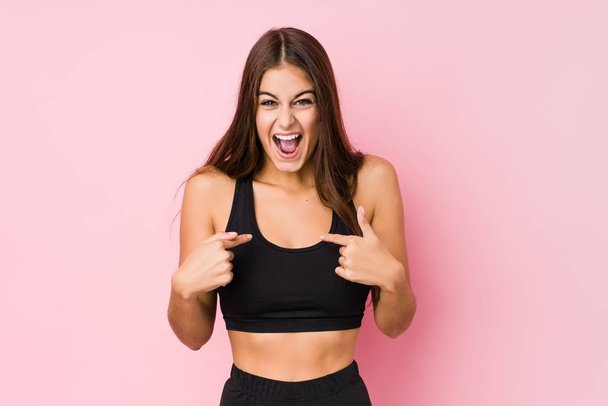 Jovem caucasiano fitness mulher fazendo esporte isolado surpreso apontando com o dedo, sorrindo amplamente
. - Foto, Imagem