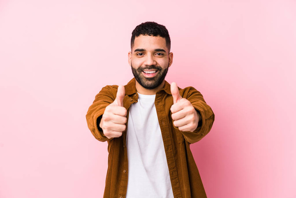 Young latin man against a pink background isolated with thumbs ups, cheers about something, support and respect concept. - Photo, Image