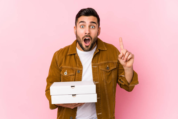 Jeune homme beau tenant des pizzas isolé ayant une idée, concept d'inspiration
. - Photo, image