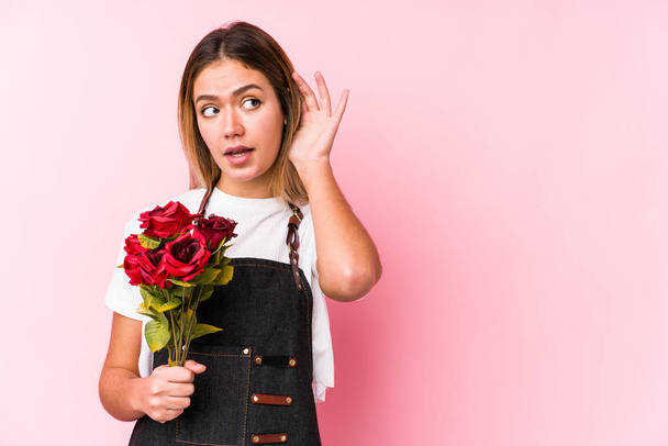 Giovane donna caucasica in possesso di un rose isolato cercando di ascoltare un pettegolezzo
. - Foto, immagini
