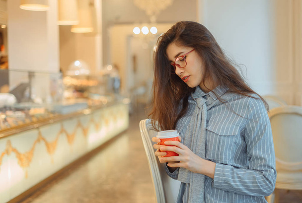 junge asiatische Frau im Café hält Heißgetränk in Pappbecher - Foto, Bild