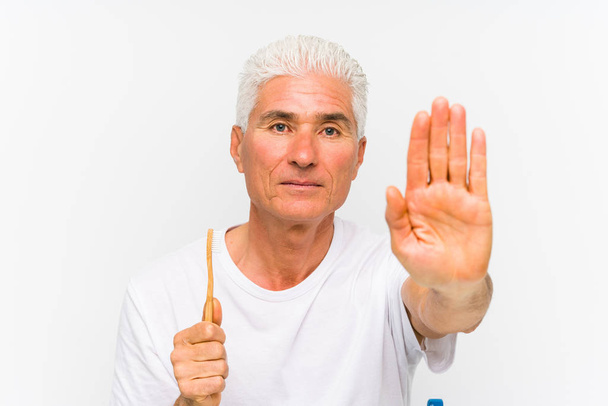 Starší běloch, který drží zubní kartáček izolovaný, stojí s nataženou rukou a ukazuje stopku.. - Fotografie, Obrázek