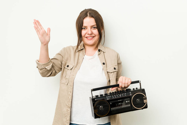 Jonge bochtige vrouw met een retro radio ontvangen van een aangename verrassing, opgewonden en het verhogen van de handen. - Foto, afbeelding