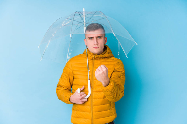 Молодой кавказский мужчина с зонтиком, показывающим кулак к камере, агрессивное выражение лица
. - Фото, изображение