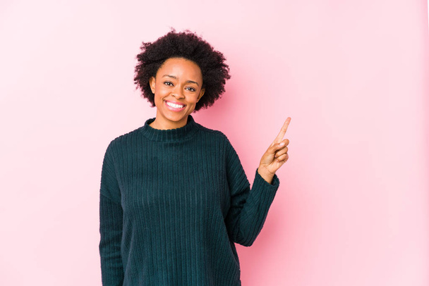 中年アフリカ系アメリカ人女性に対してピンクの背景隔離された笑顔陽気に指していますとともに前指離れて. - 写真・画像
