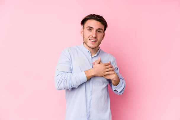 Junger kaukasischer Mann, der isoliert auf rosa Hintergrund posiert, hat freundlichen Gesichtsausdruck und drückt die Handfläche auf die Brust. Liebeskonzept. - Foto, Bild
