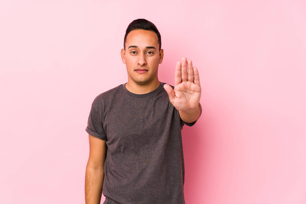Yooung latin man posing in a pink backgroundstanding with outstretched hand showing stop sign, preventing you. - Photo, Image