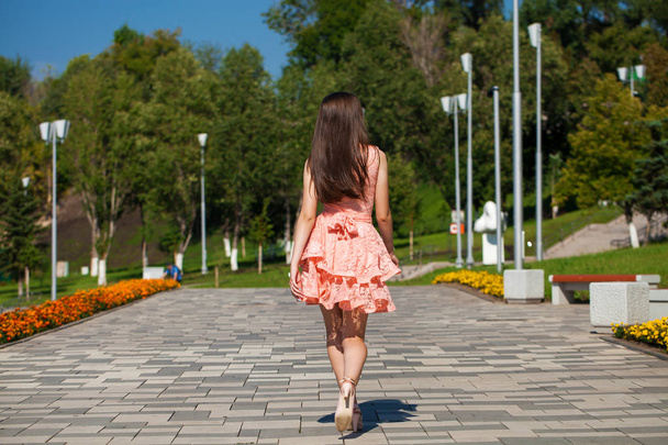 Young beautiful woman in pink dress walking on the summer street - 写真・画像