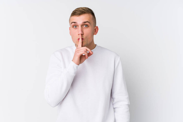 Νεαρός Καυκάσιος άντρας σε λευκό φόντο κρατώντας μυστικό ή ζητώντας σιωπή. - Φωτογραφία, εικόνα