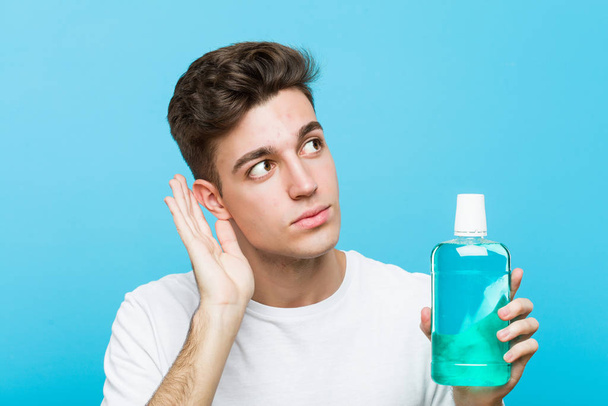 Young caucasian man holding a mouthwash trying to listening a gossip. - Photo, Image