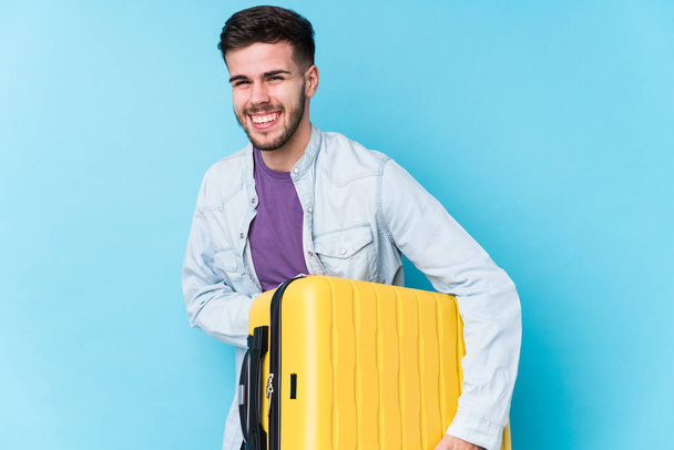 Young caucasian traveler man holding a suitcase isolated laughing and having fun. - Fotó, kép