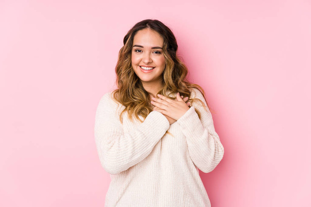 Young curvy woman posing in a pink background isolated has friendly expression, pressing palm to chest. Love concept. - Photo, Image