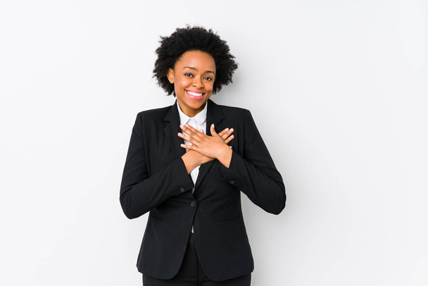 Μεσήλικας αφροαμερικανίδα επιχειρηματίας σε ένα λευκό φόντο απομονωμένη έχει φιλική έκφραση, πιέζοντας παλάμη στο στήθος. Έννοια αγάπης. - Φωτογραφία, εικόνα