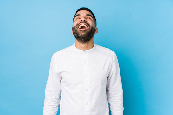 Fiatal latin férfi ellen kék háttér elszigetelt nyugodt és boldog nevetés, nyak kinyújtott bemutató fogak. - Fotó, kép