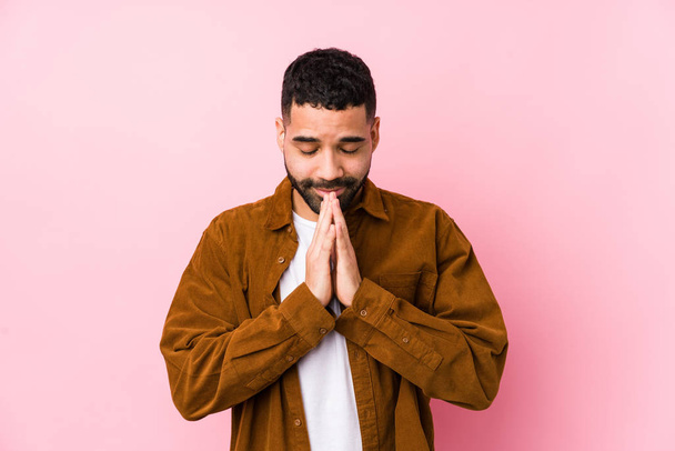 Fiatal latin férfi ellen rózsaszín háttér elszigetelt kézen imádkozni közel száj, úgy érzi, magabiztos. - Fotó, kép