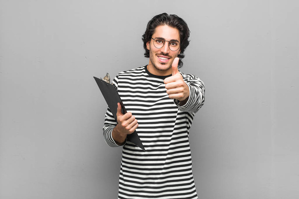 Young employee man holding an inventory with thumbs ups, cheers about something, support and respect concept. - Photo, Image