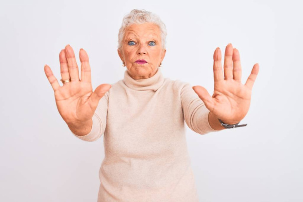 Mujer mayor de cabello gris que usa suéter de cuello alto de pie sobre un fondo blanco aislado haciendo un gesto de stop con palmas de las manos, expresión de enojo y frustración
 - Foto, imagen