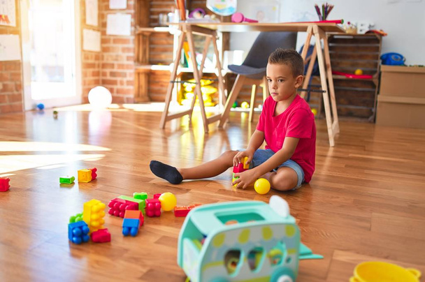 Красивый ребенок играет со строительными блоками вокруг много игрушек в детском саду
 - Фото, изображение