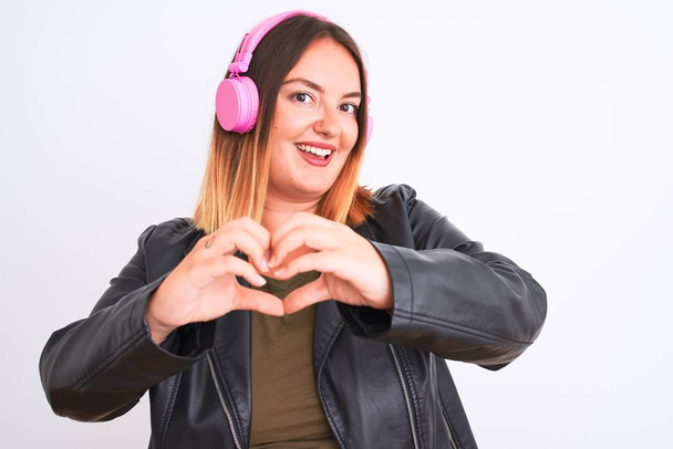 Young beautiful woman listening to music using headphones over isolated white background smiling in love showing heart symbol and shape with hands. Romantic concept. - Foto, Imagem