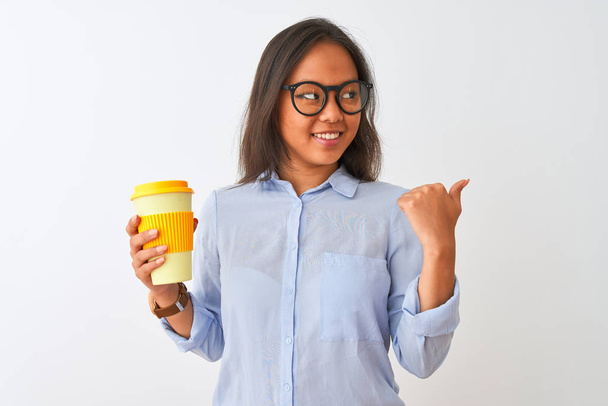 Giovane donna cinese indossa occhiali che tengono il bicchiere di caffè su sfondo bianco isolato che punta e mostra con il pollice verso l'alto sul lato con il viso felice sorridente
 - Foto, immagini