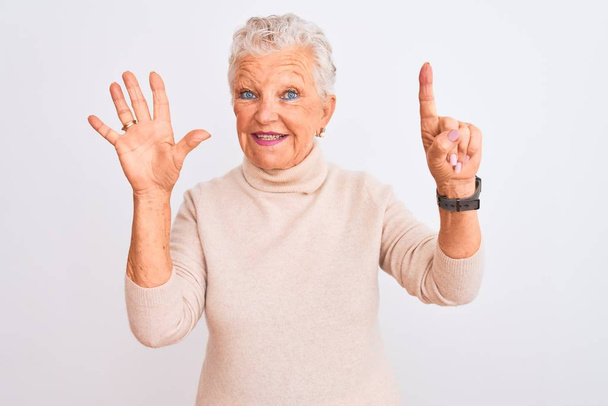 Donna anziana dai capelli grigi indossa maglione dolcevita in piedi su sfondo bianco isolato mostrando e indicando con le dita numero sei, sorridendo fiducioso e felice
. - Foto, immagini