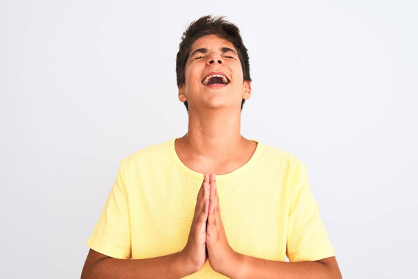 Handsome teenager boy standing over white isolated background begging and praying with hands together with hope expression on face very emotional and worried. Asking for forgiveness. Religion concept. - Photo, Image