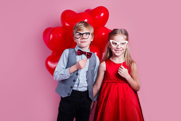 Small loving couple of kids with red heart balloons on pink background. Valentines day concept. - 写真・画像