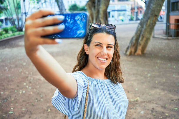 夏の晴れた日にスマートフォンを使って自画撮りをする緑の公園で幸せと陽気な笑顔の若い女性 - 写真・画像