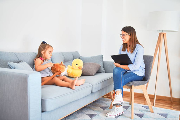 Young therapist woman speaking and treating child, counselor and behaviour correction at pedagogue payroom taking notes on clipboard - Foto, Imagem