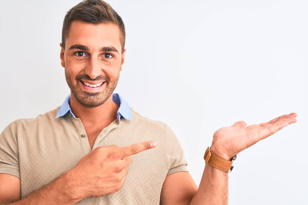 Молодой красивый мужчина в элегантной футболке на изолированном фоне очень счастлив указывая рукой и пальцем
 - Фото, изображение